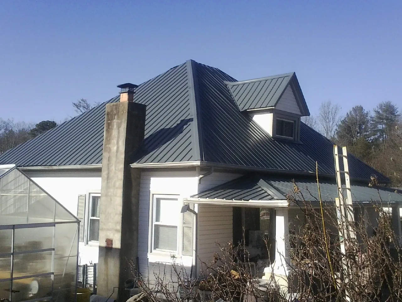 Dark blue standing seam metal roof on a white farmhouse with dormer — Slate & Tile Roof Repair by Roofing Brothers in Kendalia