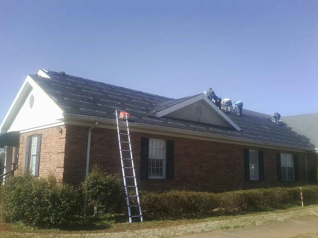 Crew tearing shingles off a brick ranch roof with a ladder set — Metal Roof Repair work by our crew in Kendalia