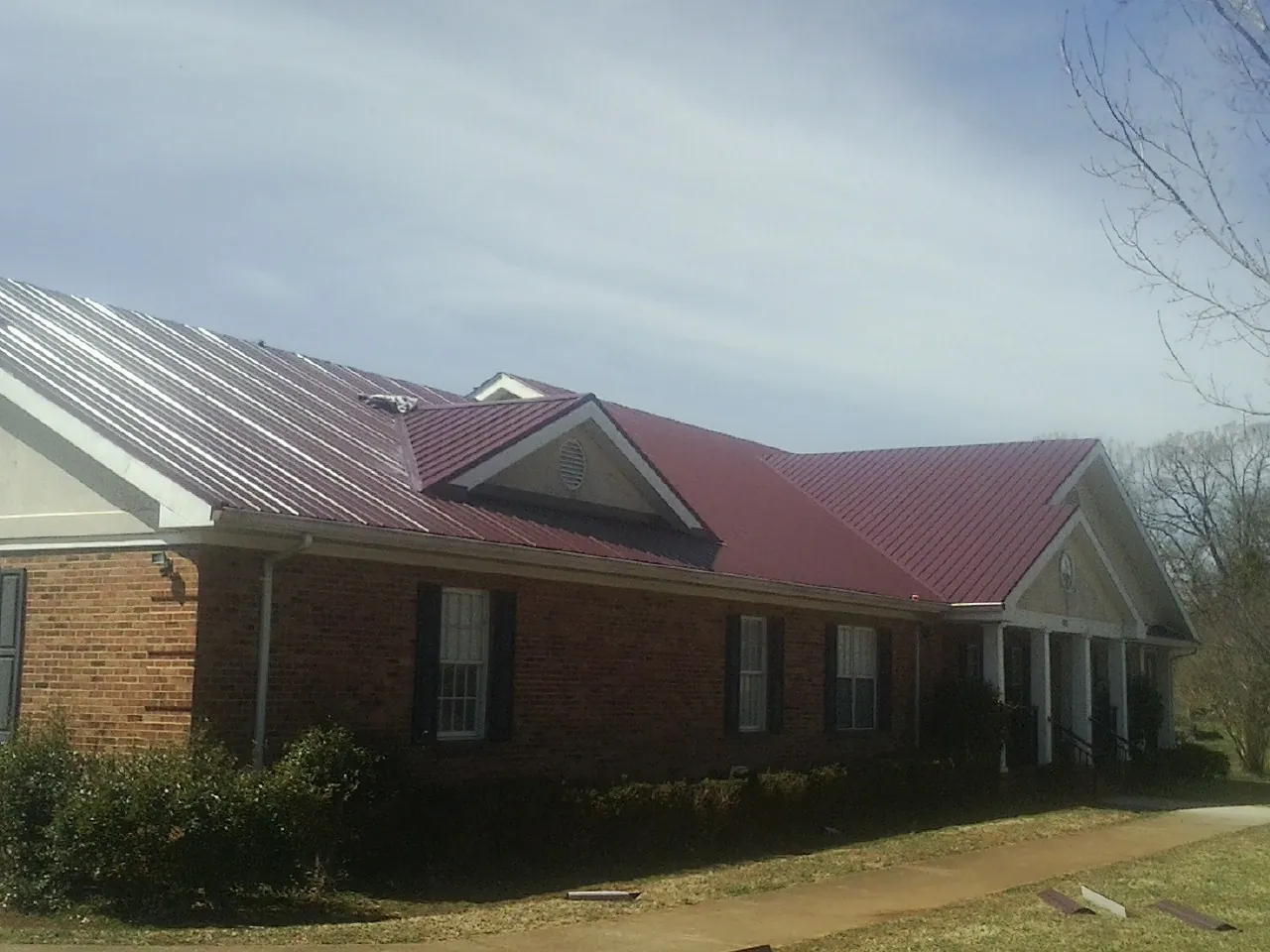 Red metal roof with gabled entries on a long brick building, from a Hail Damage Roof Repair job in Kendalia