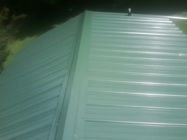 New green metal panels meeting at the ridge of a roof — Flat Roof Repair work by our crew in Kendalia