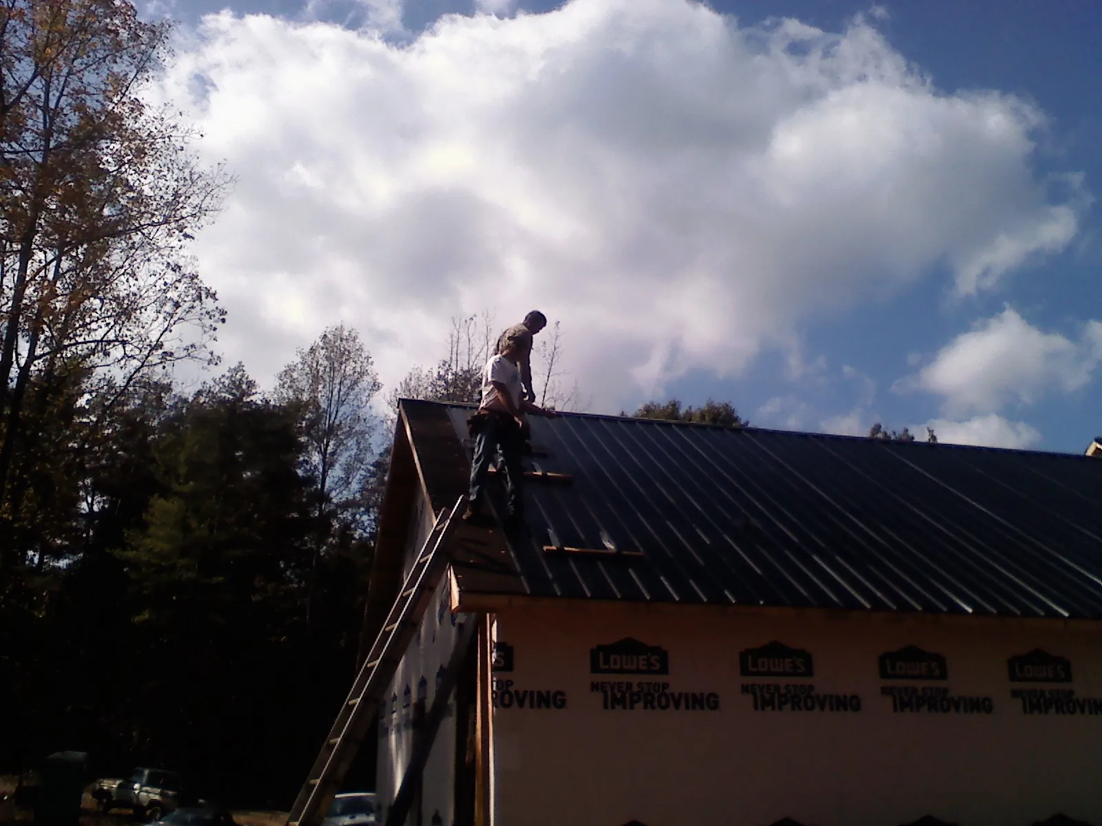 Roofer fastening dark metal panels high against a cloudy sky, from a Roof Inspection job in Kendalia