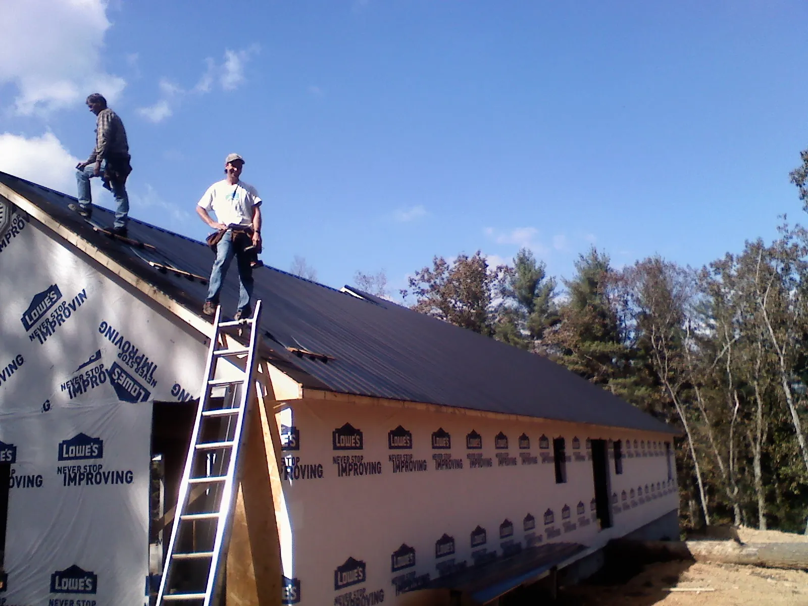 Two roofers standing on a long dark metal roof over a wrapped building in Kendalia
