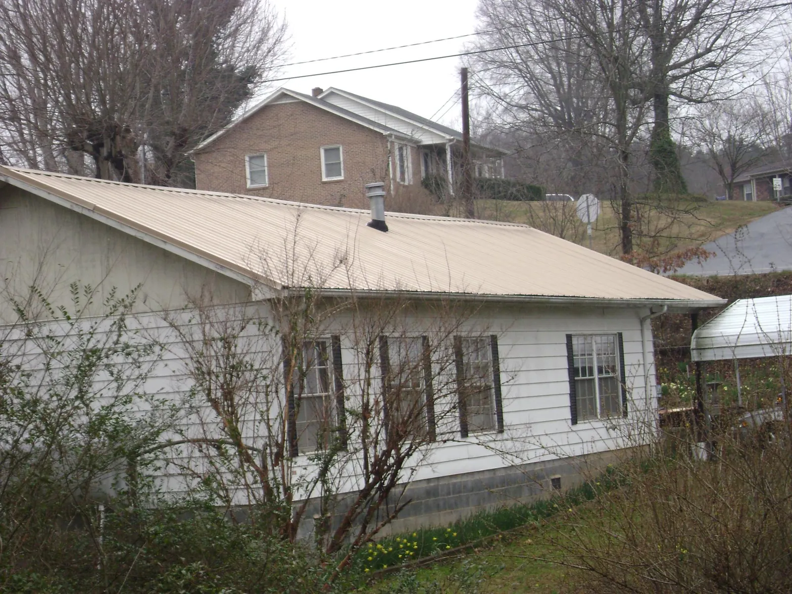 Tan metal roof on a white sided house set into a hillside — Commercial Roofing by Roofing Brothers in Kendalia