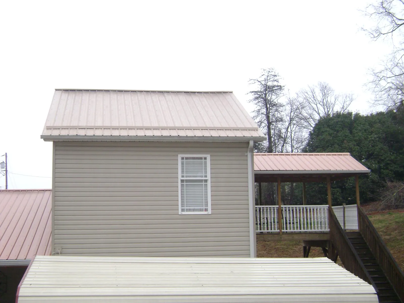 Tan metal roofs on a two story addition and attached porch, from a Roof Replacement job in Kendalia